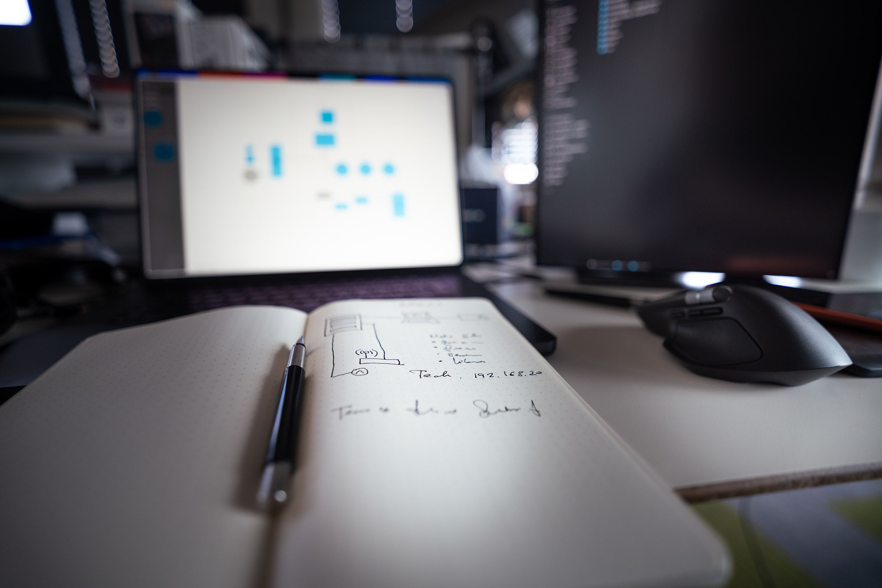 Minimalistyczne studio: otwarty notes, długopis i zielona roślina na drewnianym biurku.